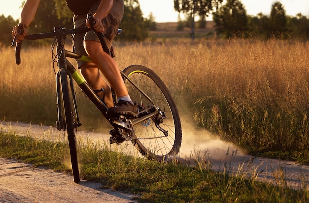 Zdjęcie rowerzysta na rowerze podnosi kurz z tylnego koła po poślizgu na polu o zachodzie słońca.