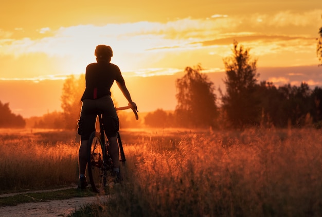 Zdjęcie rowerzysta na rowerze szutrowym stoi w polu na pięknym tle zachodu słońca.