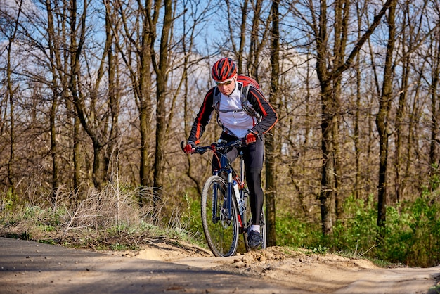 Rowerzysta sportowy jeździ szlakiem w lesie w słoneczny wiosenny dzień.