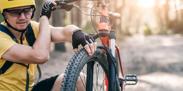 Rowerzysta sprawdzający ciśnienie przedniego koła roweru w słonecznym lesie