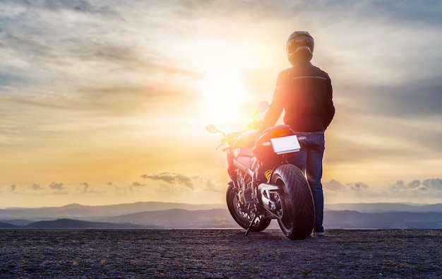 Rowerzysta stojący obok motocykla obserwujący zachód słońca