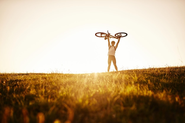 Rowerzysta trzyma rower nad sobą na tle czerwonego zachodu słońca Rowerzysta z rowerem na polu podczas wschodu słońca