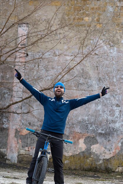 Rowerzysta w krótkich spodenkach i koszulce na nowoczesnym karbonowym rowerze hardtail z widelcem pneumatycznym stojącym na klifie na tle świeżego zielonego wiosennego lasu