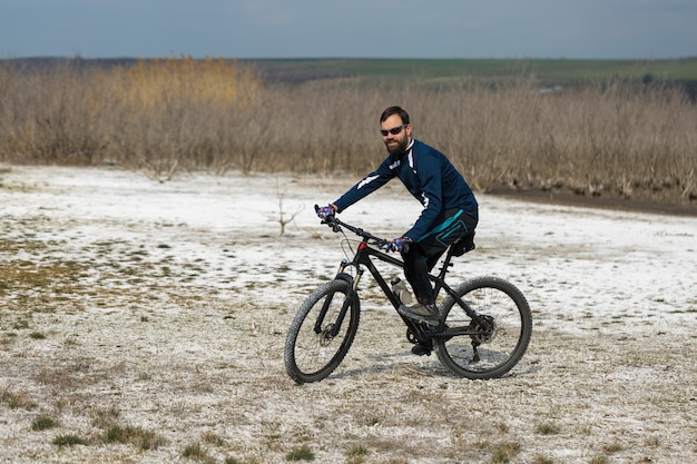 Rowerzysta w krótkich spodenkach i koszulce na nowoczesnym rowerze z widelcem pneumatycznym stojącym na klifie
