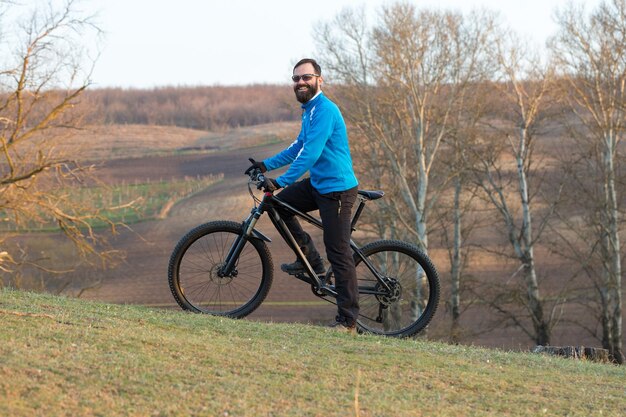 Rowerzysta w spodniach i polarowej kurtce na nowoczesnym rowerze hardtail z włókna węglowego z widelcem pneumatycznym Facet na szczycie wzgórza jeździ na rowerze