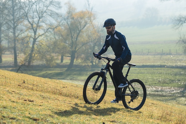 Rowerzysta w spodniach i polarowej kurtce na nowoczesnym rowerze hardtail z włókna węglowego z widelcem pneumatycznym. Facet na szczycie wzgórza jeździ na rowerze.