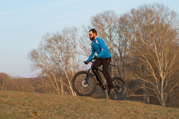 Rowerzysta w spodniach i polarowej kurtce na nowoczesnym rowerze hardtail z włókna węglowego z widelcem pneumatycznym