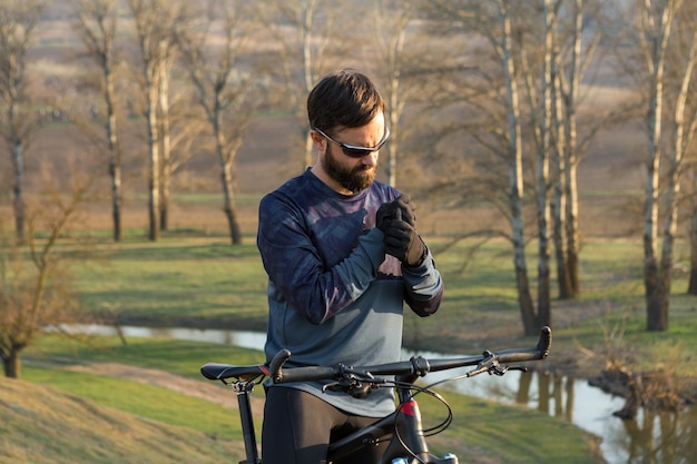 Rowerzysta w szortach i koszulce na nowoczesnym karbonowym rowerze hardtail z widelcem pneumatycznym stojącym na klifie na tle świeżego zielonego wiosennego lasu