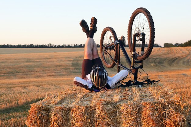 Zdjęcie rowerzysta z rowerem odpoczywa na polu ze słomy