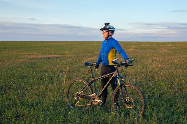 Zdjęcie rowerzysta z rowerem odpoczywa na zielonym polu na tle błękitnego nieba. sport i rekreacja na łonie natury