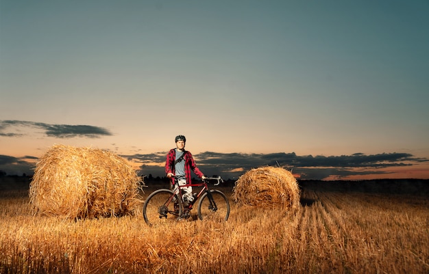 Rowerzysta z stojakami rowerowymi w polu bel słomy o zachodzie słońca.