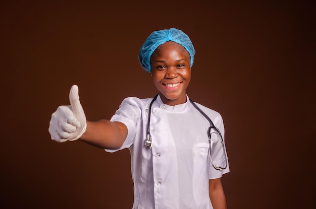 Rozbawiona i pod wrażeniem afrykańska lekarka pielęgniarka w fartuchach i pokazująca kciuk w aprobacie zgadzam się lub komplementuję pracę