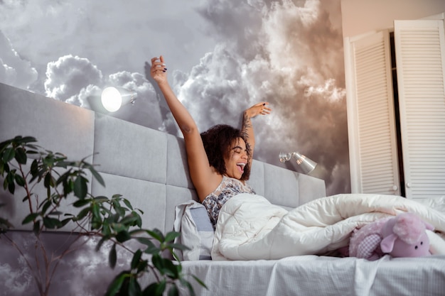 Rozciąganie I Ziewanie. Spokojna Ciemnowłosa African American Kobieta W Piżamie, Siedząc W łóżku