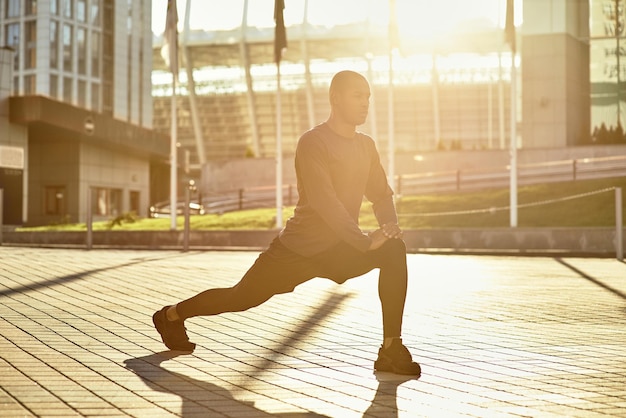 Rozciąganie po świetnym treningu widok z boku sportowca rozciągającego nogi podczas porannego treningu w słońcu