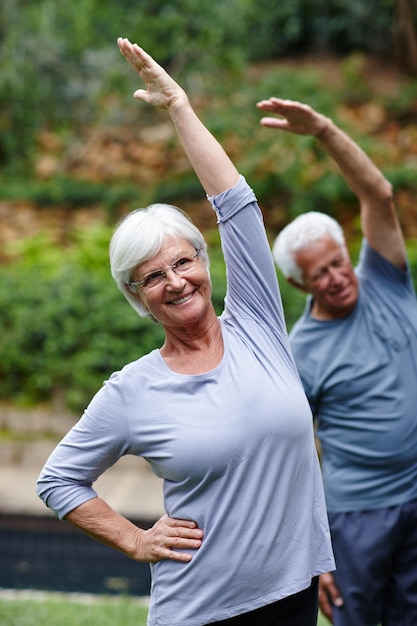 Zdjęcie rozciąganie w kierunku zdrowia i szczęścia ujęcie starszej pary ćwiczącej razem jogę na świeżym powietrzu