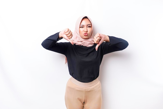 Rozczarowana azjatycka muzułmanka ubrana w hidżab daje kciuk w dół gestem dezaprobaty odizolowanym białym tłem