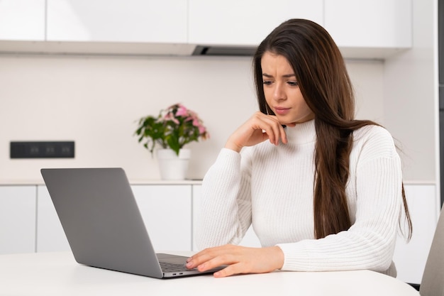 Rozczarowana kobieta czuje się beznadziejnie w pracy siedząc przy biurku i korzystając z laptopa