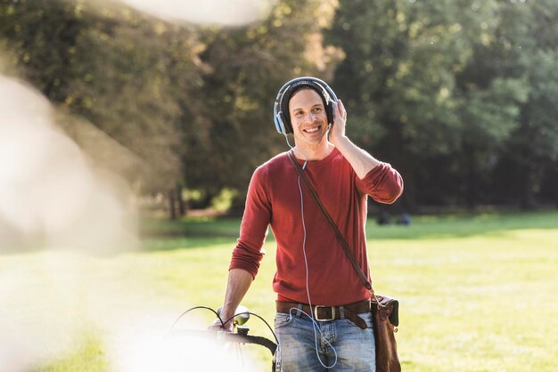 Roześmiany mężczyzna słuchający muzyki ze słuchawkami w parku z wyścigowym cyklem