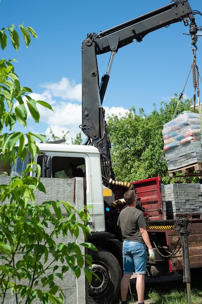 Rozładunek płyt chodnikowych z ciężarówki Mężczyźni rozładowują płyty chodnikowe za pomocą manipulatora Pracownicy rozładowują materiały budowlane z dużej maszyny