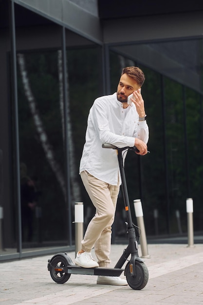 Rozmowa przez telefon Stylowy mężczyzna jest ze swoim skuterem na świeżym powietrzu w ciągu dnia