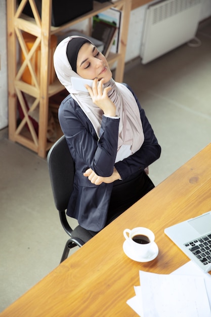 Rozmowa przez telefon, uwzględniona. Piękna arabska kobieta nosi hidżab podczas pracy na openspace lub w biurze. Pojęcie zawodu, wolności w biznesie, przywództwa, sukcesu, nowoczesnego rozwiązania.