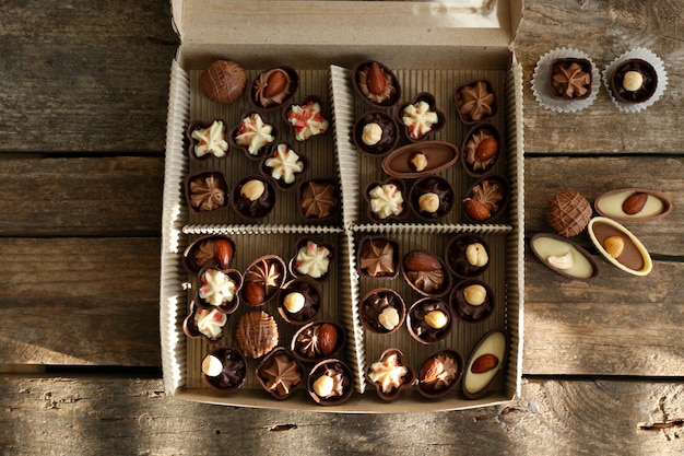Różne cukierki czekoladowe w papierowym pudełku na drewnianym tle, z bliska