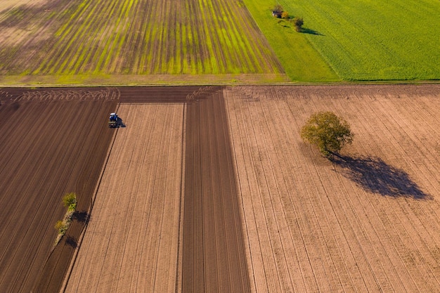 Różne kolory pól i gruntów ornych z ciągnikiem, a także drzewa i paski kwiatów