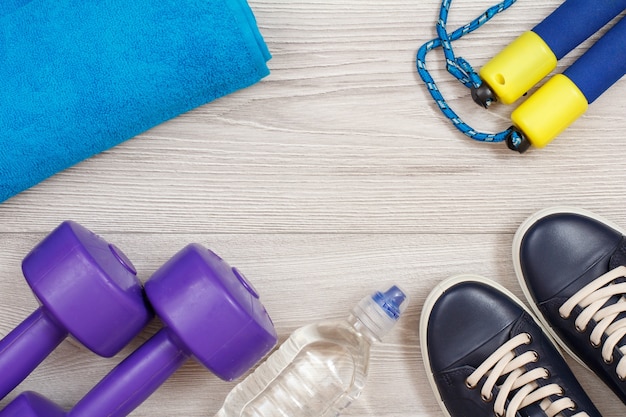 Różne narzędzia do fitnessu z butelką wody i ręcznikiem w pokoju lub siłowni na szarej podłodze.