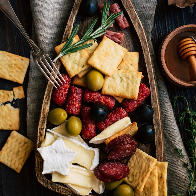 Różne przekąski na drewnianej desce do krojenia, serze, krakersy, salami, oliwki