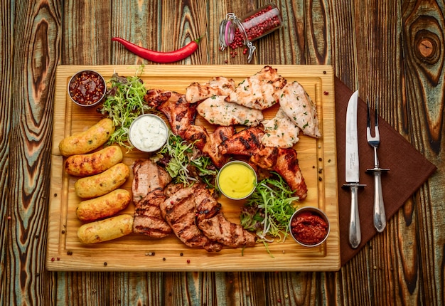Różne pyszne grillowane mięso i warzywa ze świeżą sałatką i sosem bbq na desce do krojenia na drewnianym stole