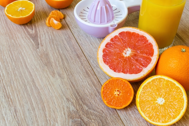 Różne ręczne rozwiertaki do całych i pokrojonych owoców cytrusowych i szklanka soku pomarańczowego na drewnianym stole