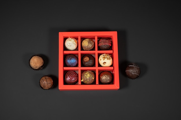 Różne ręcznie robione cukierki czekoladowe truflowe w czerwonym pudełku na ciemnym tle. Bezpośrednio nad widokiem z góry.