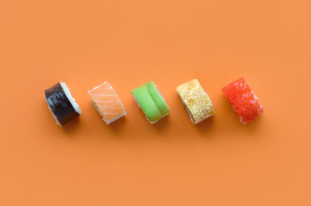 Różne rodzaje azjatyckich rolek sushi na pomarańczowym tle Minimalizm widok z góry płaski leżał z japońskim jedzeniem