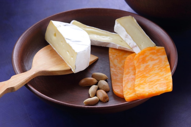 Różne rodzaje kompozycji serów na niebieskim tle zbliżenie Sery z orzechami i drewnianą łopatką na glinianym talerzu