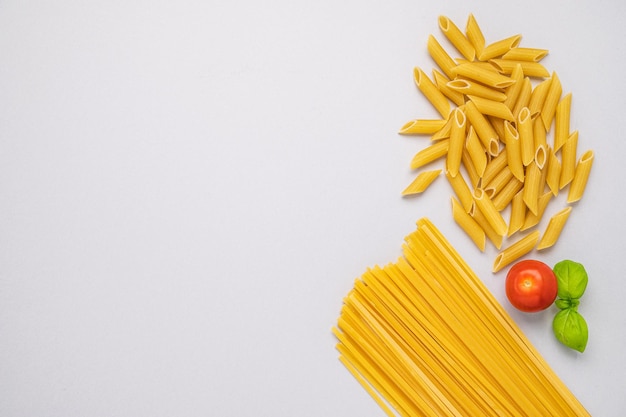 Różne rodzaje makaronów na szarym tle Spaghetti i penne z pomidorami i bazylią