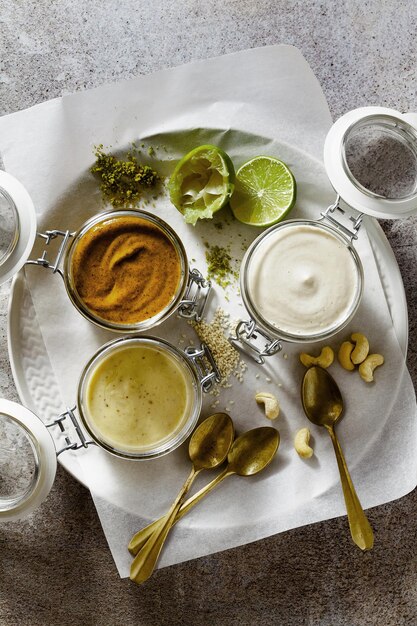 Różne rodzaje sosów w szklanych słoikach z pistacjami, orzechami nerkowca i wegańskim majonezem na kamiennym tle