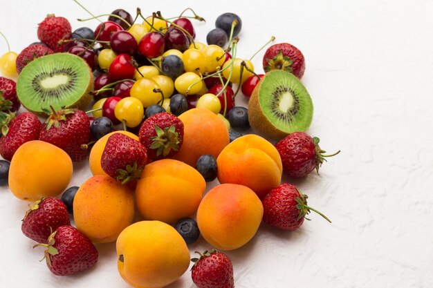 Różne świeże jagody i owoce. Morele Kiwi Truskawka Wiśnia Jagoda na białym stole