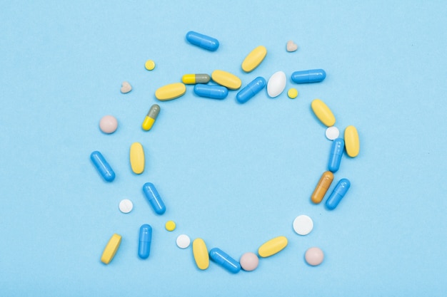 Różne tabletki i kapsułki w formie serca na niebieskim tle. Widok z góry