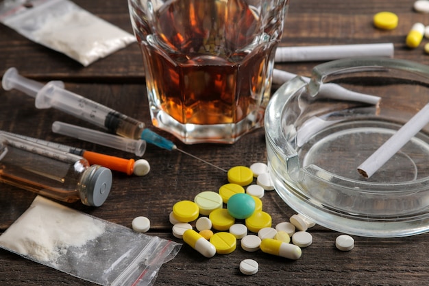 Różne uzależniające narkotyki, w tym alkohol, papierosy i narkotyki na brązowym drewnianym stole. Koncepcja uzależnienia od narkotyków
