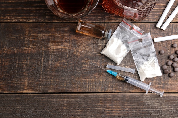 Różne uzależniające narkotyki, w tym alkohol, papierosy i narkotyki na brązowym drewnianym stole. widok z góry z miejscem na tekst