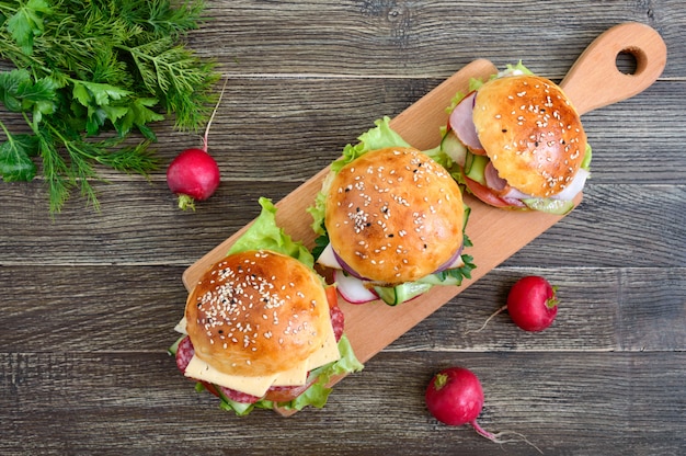 Różni Hamburgery Na Drewnianej Desce. Domowa Bułka Z Szynką Lub Mięsem Lub Salami, Warzywami, Ziołami. Kanapki Na Lunch. Widok Z Góry