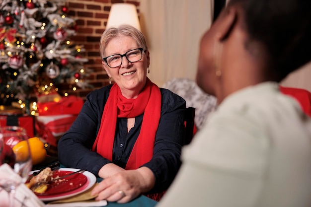 Różnorodne kobiety rozmawiają przy świątecznym stole, jedząc tradycyjne potrawy. Obchody ferii zimowych w pięknie urządzonym miejscu, ludzie zbierają się na świątecznej imprezie domowej