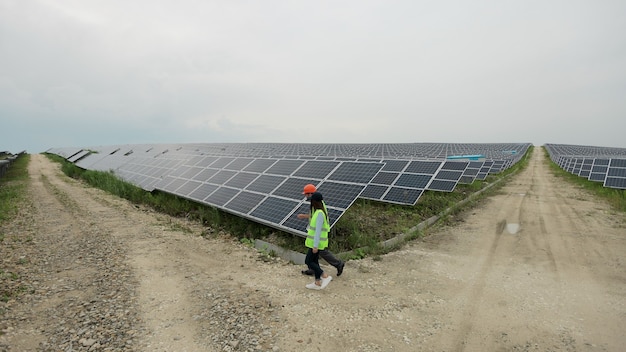 Różnorodni inżynierowie w specjalnych mundurach spacerują po farmie fotowoltaicznej. Rzędy baterii słonecznych. Koncepcja zielonej energii. Pole paneli słonecznych.