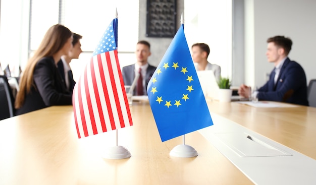 Różnorodni ludzie rozmawiają o międzynarodowym partnerstwie konferencyjnym. Flaga amerykańska i flaga Unii Europejskiej.