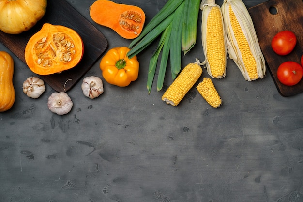 Różnorodność dojrzałych warzyw, w tym dyni i kukurydzy na ciemnym tle stołu