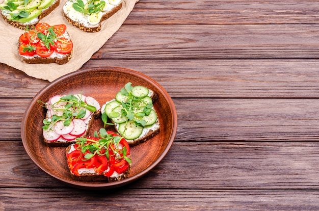 Różnorodność mini kanapek z twarogiem i warzywami na glinianej tarce i papierem na drewnianej powierzchni