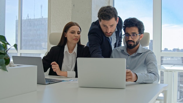 Różnorodny zespół współpracowników korporacyjnych pracujących z laptopami w biurze męski trener biznesu mentor szef
