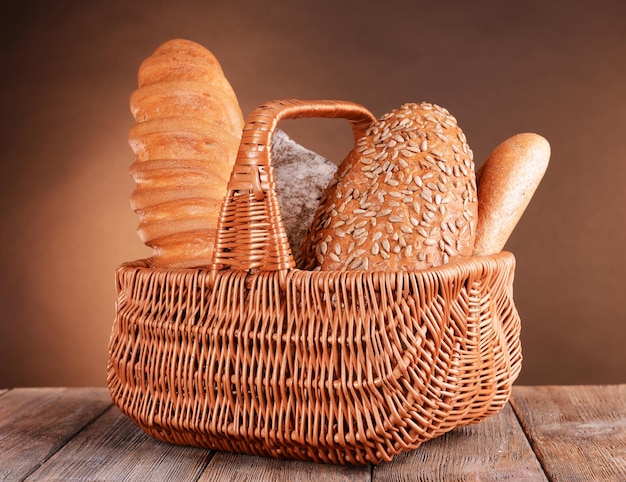 Różny chleb w wiklinowym koszu na stole na brązowym tle
