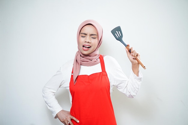 Rozochocona azjatycka muzułmańska kobieta trzyma łopatkę w czerwonym fartuchu Naczynia do gotowania Koncepcja gotowania