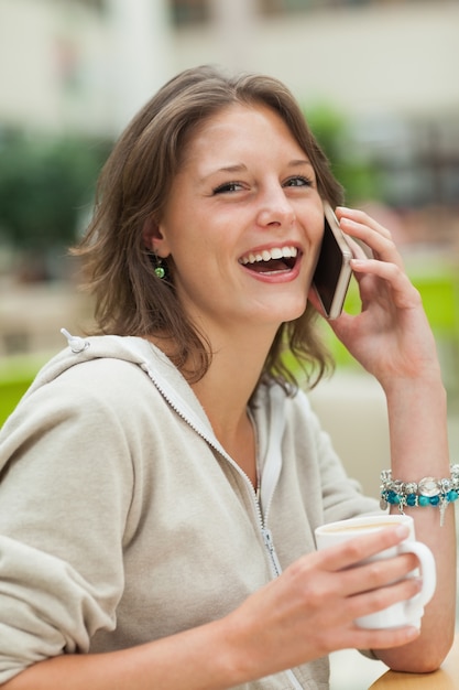 Rozochocona kobieta używa telefon komórkowego podczas gdy pijący kawę